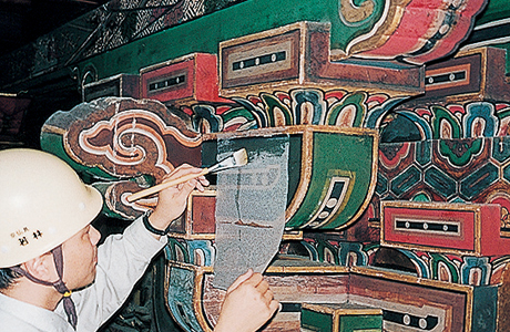 剥落止め工事作業風景　彩色表面を湿らせた後、修復部分の表面に和紙を水貼りする